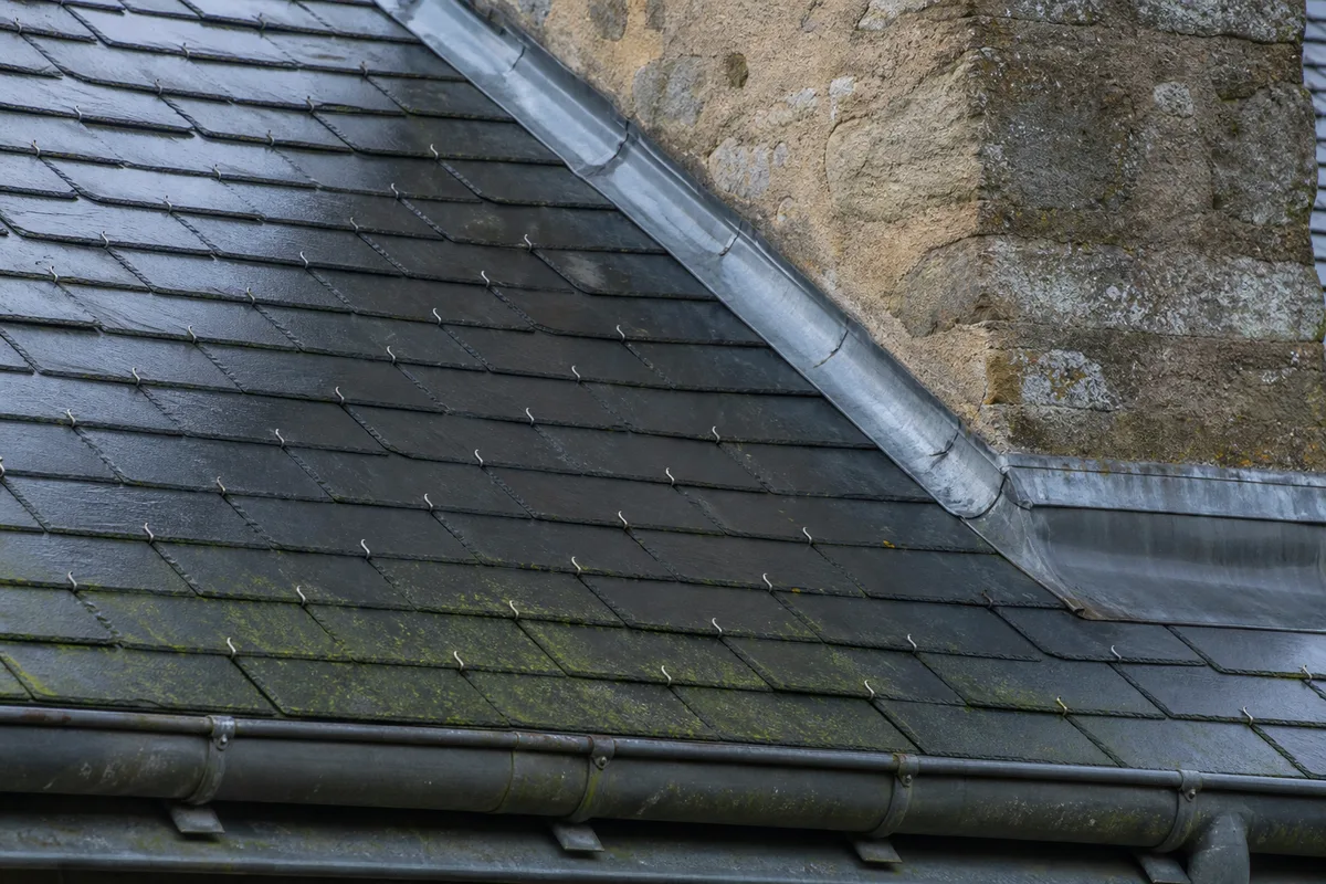 Toiture en ardoise d’une maison normande du pays d’Andaines avec versant ombragé et souche de cheminée en pierre