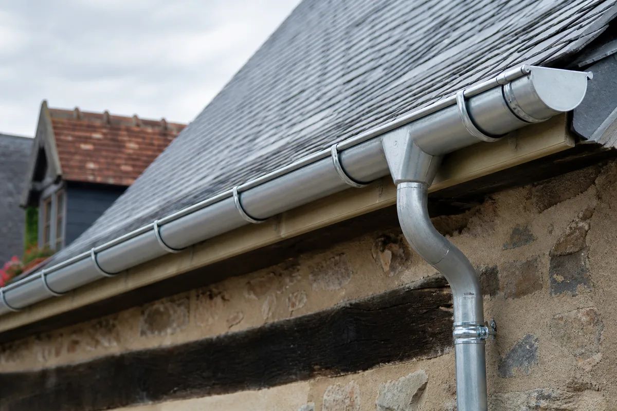 Gouttière en zinc neuve posée en bord de toiture ardoise d&rsquo;une maison normande, crochets et descente visibles